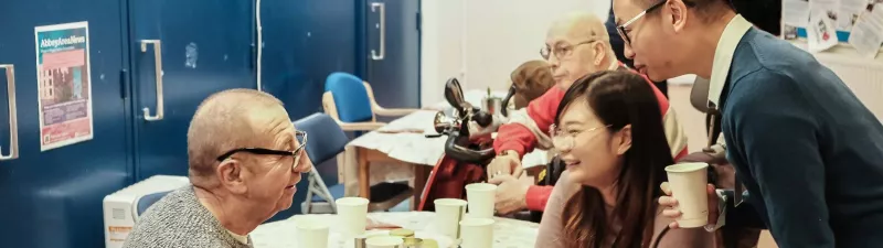 Two volunteers chat and laugh with a man at a table